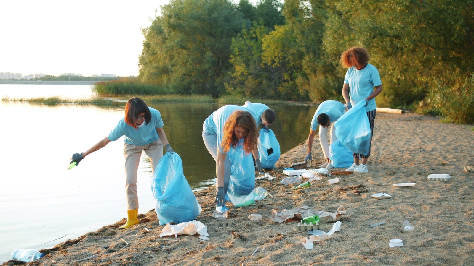 Group of volunteers cleaning a beach shoreline at sunset, promoting environmental awareness.